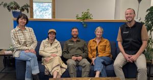 Photograph of five people sitting on a coach looking at the camera.
