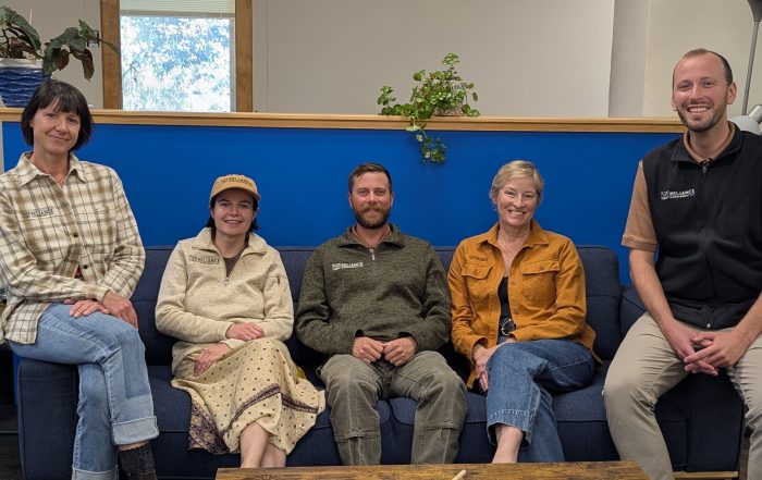 Photograph of five people sitting on a coach looking at the camera.
