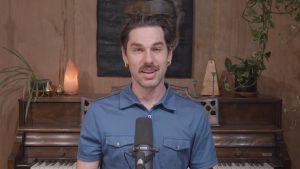 man in blue shirt sitting talking into a mircophone